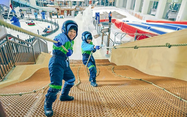 Children climbing rope hill at Snow Dunes Theme Park indoor snow area.