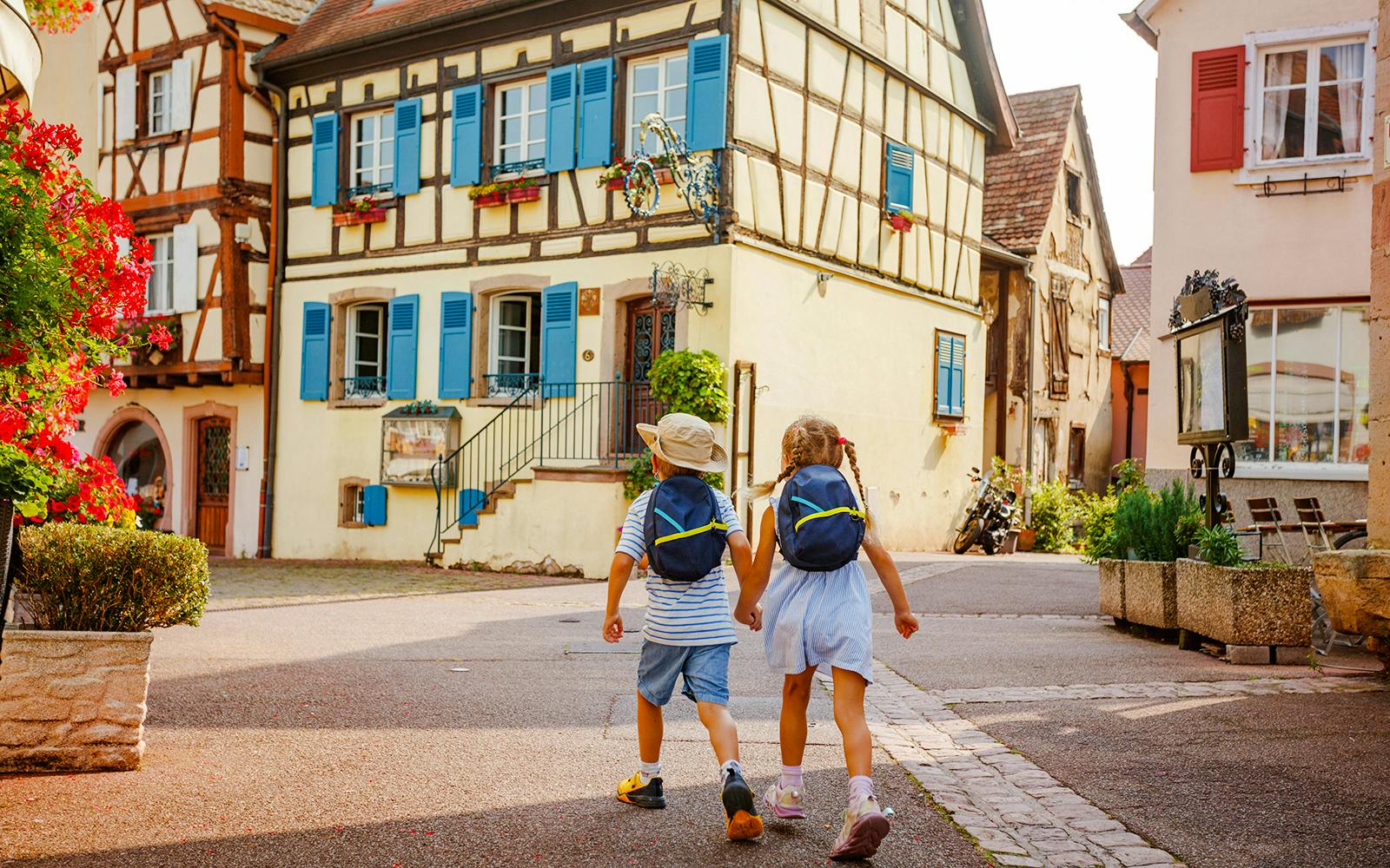 Children walking through Eguisheim village with colorful timber-framed houses.
