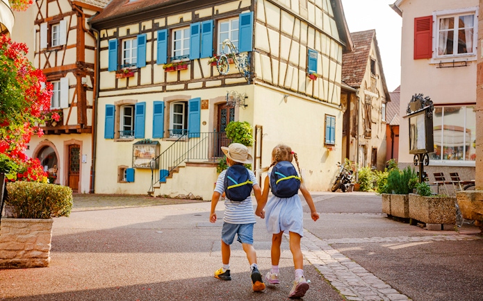 Children walking through Eguisheim village with colorful timber-framed houses.