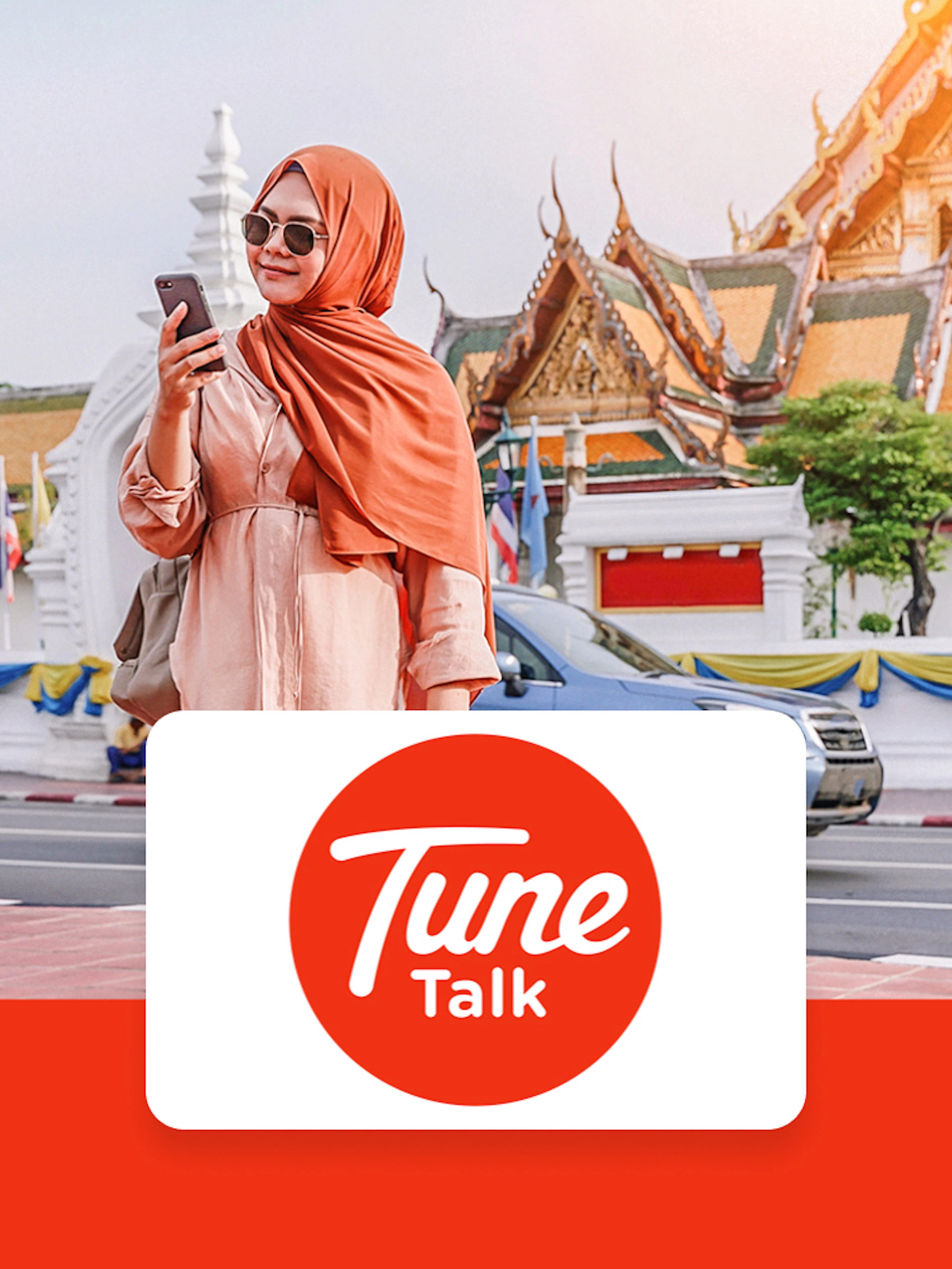Traveler using phone with Tune Talk SIM card in front of traditional architecture in Kuala Lumpur, Malaysia.
