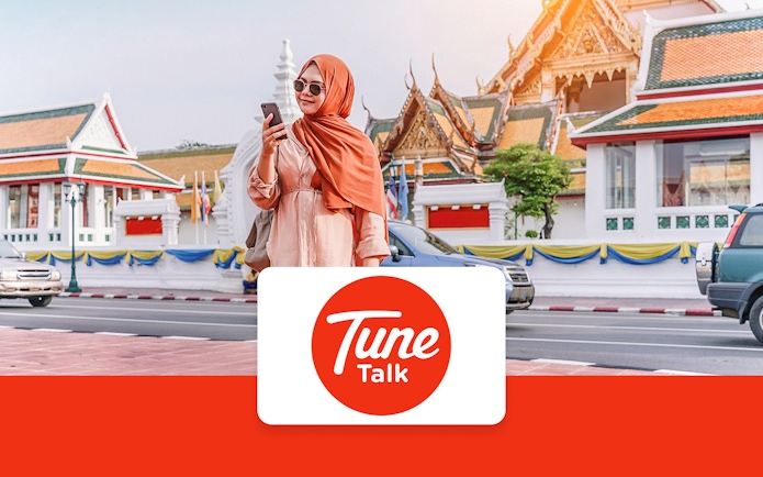 Traveler using phone with Tune Talk SIM card in front of traditional architecture in Kuala Lumpur, Malaysia.