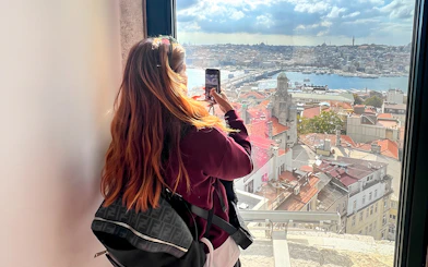 Tourist taking photo from Galata Tower overlooking Istanbul rooftops and Bosphorus.