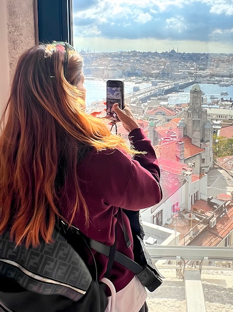 Tourist taking photo from Galata Tower overlooking Istanbul rooftops and Bosphorus.