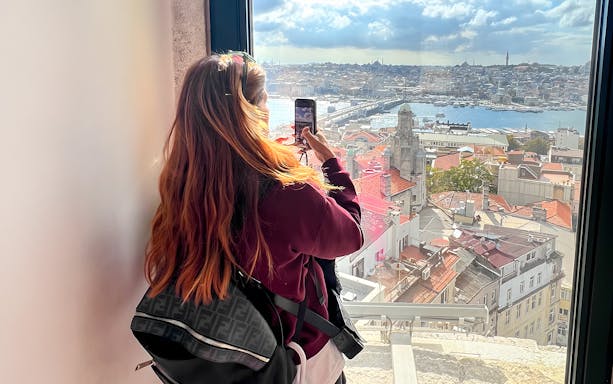 Tourist taking photo from Galata Tower overlooking Istanbul rooftops and Bosphorus.