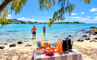 Brunch setup on Mahebourg beach with people snorkeling in Mauritius.