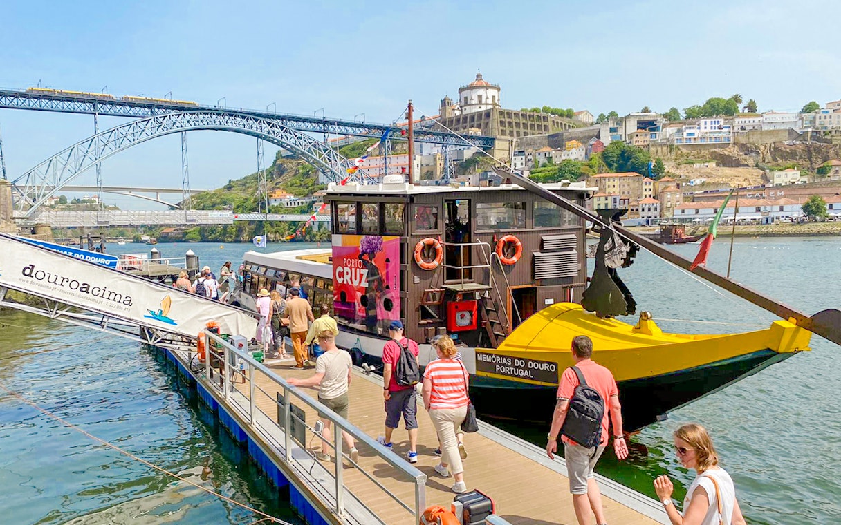 Tourists boarding a Douro River cruise in Porto, Portugal, with Dom Luís I Bridge in the background.