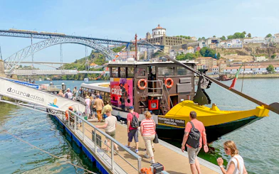 Tourists boarding a Douro River cruise in Porto, Portugal, with Dom Luís I Bridge in the background.