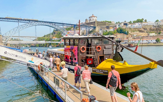 Tourists boarding a Douro River cruise in Porto, Portugal, with Dom Luís I Bridge in the background.