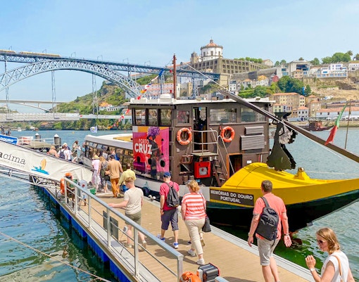 Tourists boarding a Douro River cruise in Porto, Portugal, with Dom Luís I Bridge in the background.