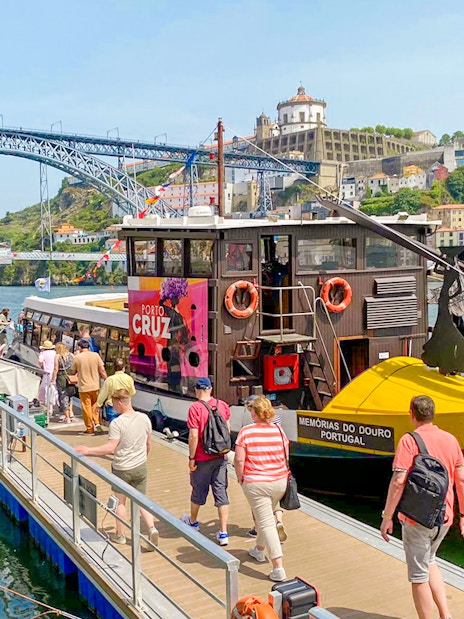 Tourists boarding a Douro River cruise in Porto, Portugal, with Dom Luís I Bridge in the background.