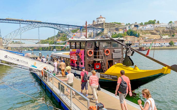 Tourists boarding a Douro River cruise in Porto, Portugal, with Dom Luís I Bridge in the background.