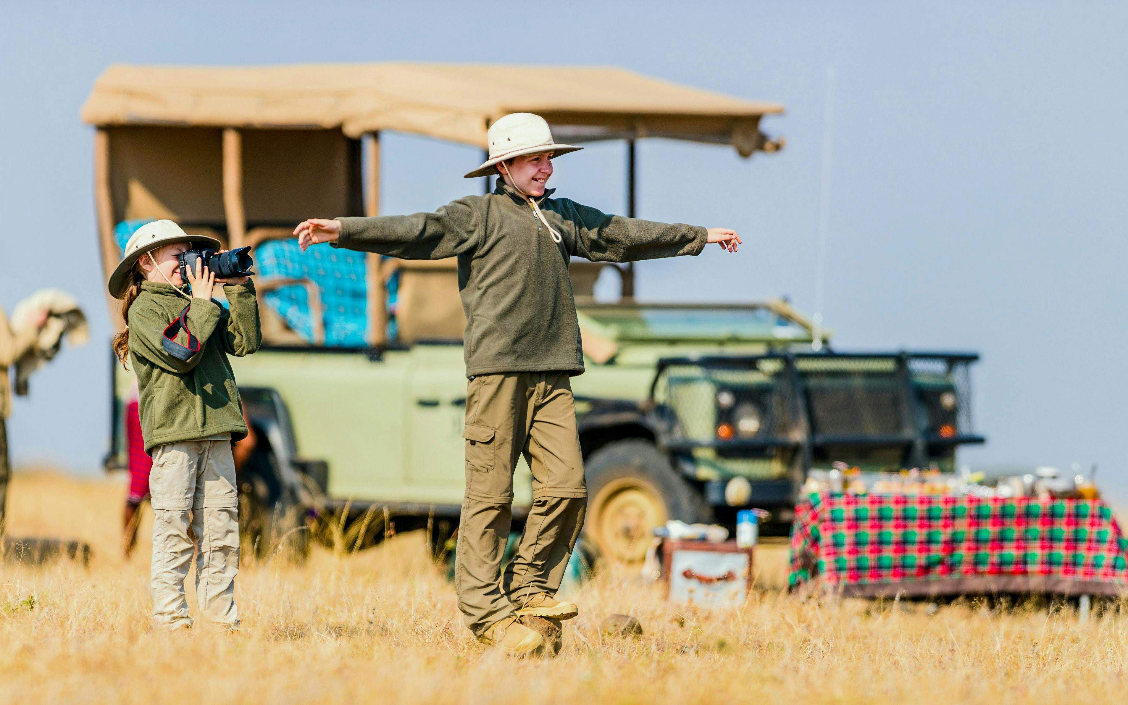 Children on safari in Africa with camera and jeep in background.