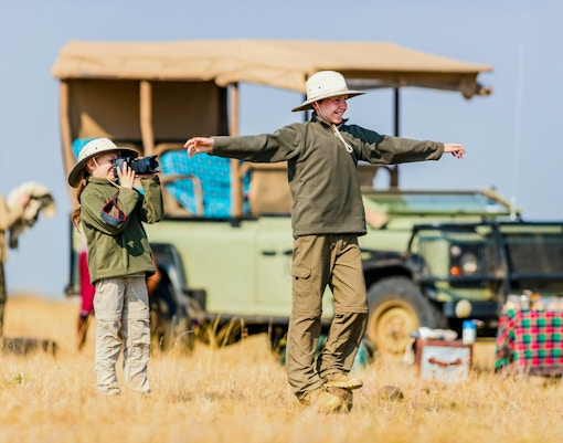 Children on safari in Africa with camera and jeep in background.