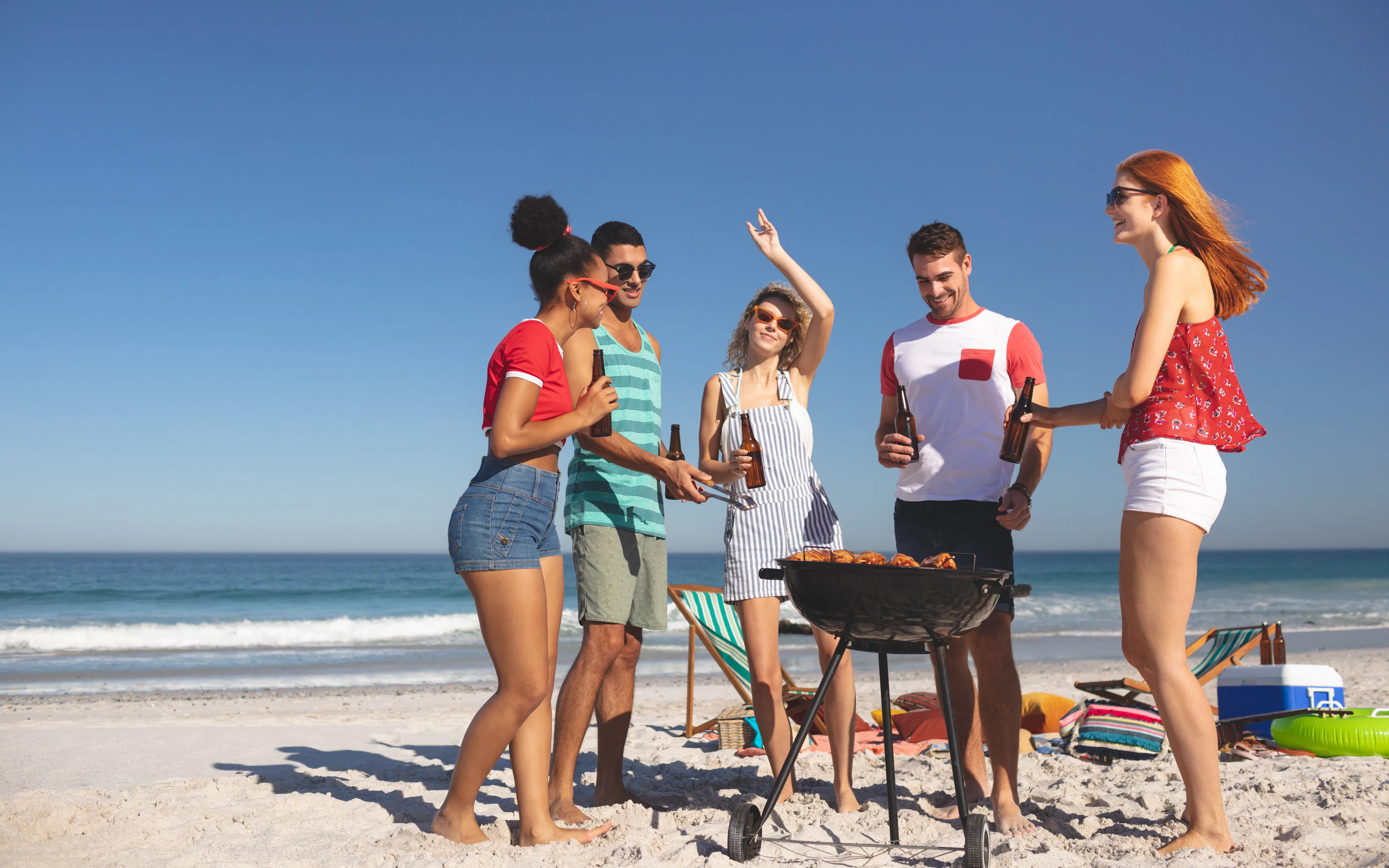 Group of friends having fun while preparing food on barbecue at beach