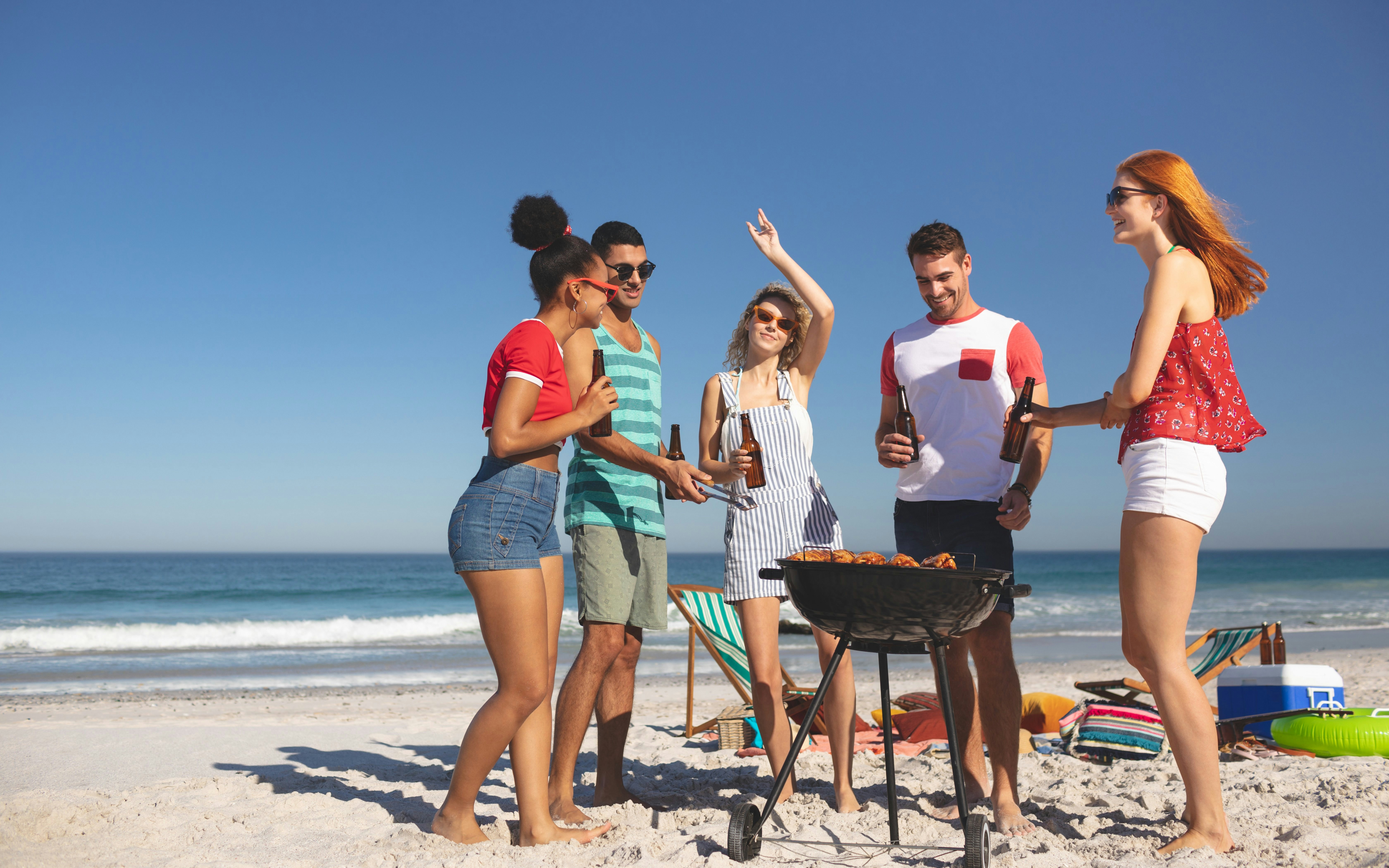 Group of friends having fun while preparing food on barbecue at beach
