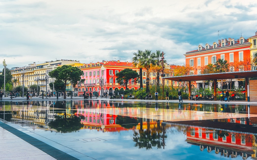 Colorful buildings and palm trees reflected in a water mirror in Nice, France.