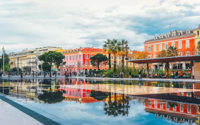 Colorful buildings and palm trees reflected in a water mirror in Nice, France.