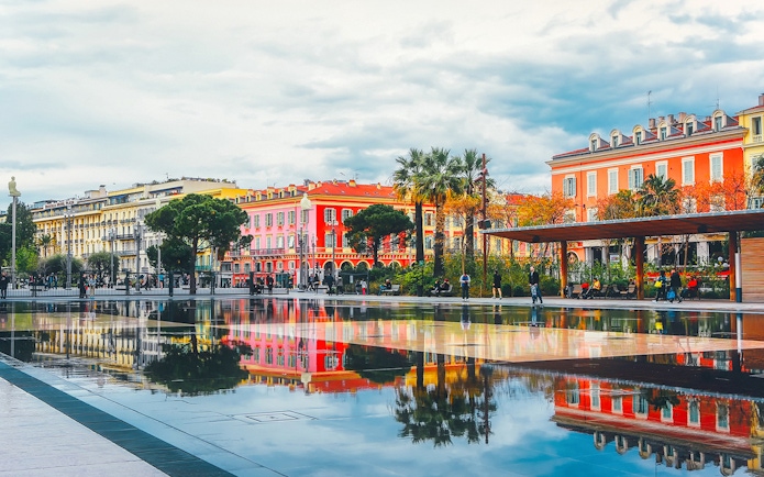Colorful buildings and palm trees reflected in a water mirror in Nice, France.