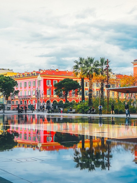 Colorful buildings and palm trees reflected in a water mirror in Nice, France.