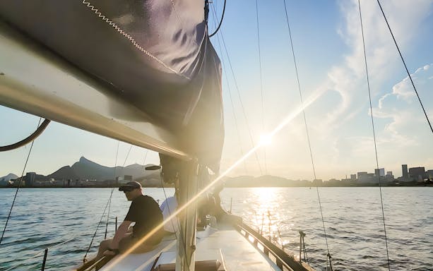 Tourist on sailboat viewing Rio de Janeiro skyline at sunset.