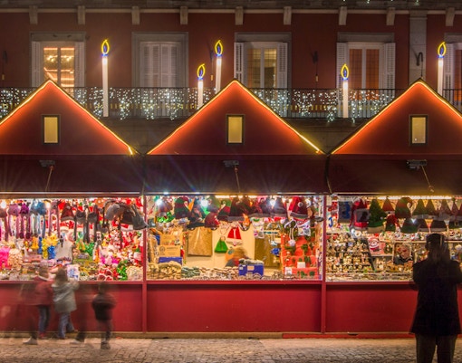 Christmas market stall with festive decorations and toys, people browsing in the evening.