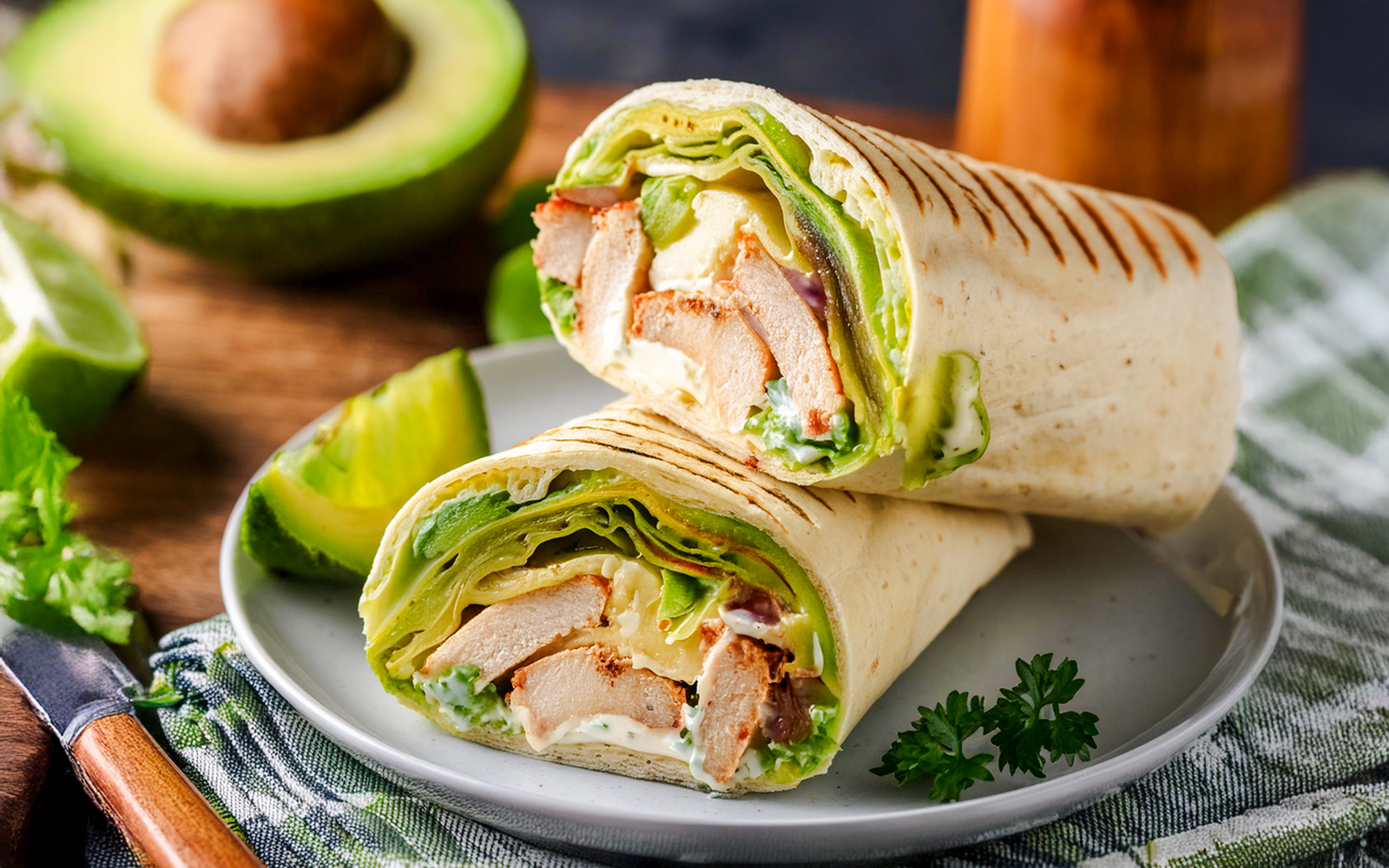 Grilled chicken avocado wrap with fresh vegetables on a wooden board.