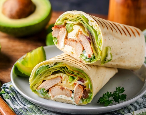 Grilled chicken avocado wrap with fresh vegetables on a wooden board.