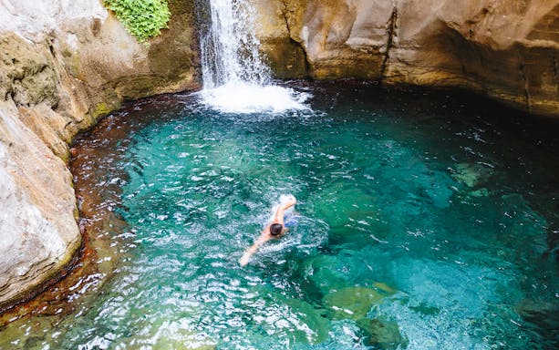 Person swimming in a clear turquoise pool beneath a waterfall in Antalya.