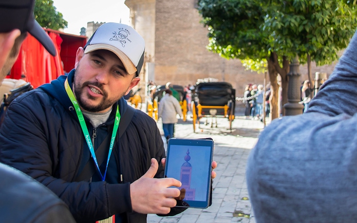 Tour guide showing a tablet with a monument image during a walking tour in Seville.