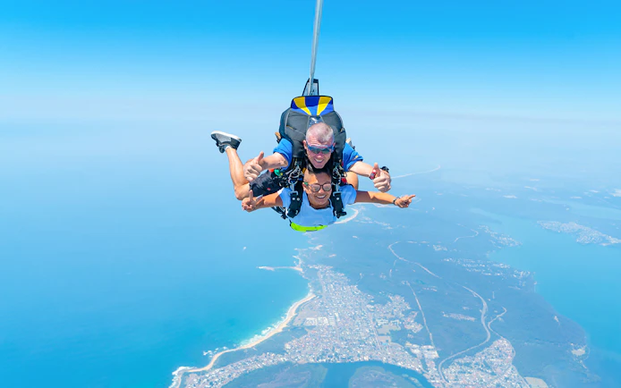 Skydivers tandem freefall over Newcastle Beach, Sydney with ocean and coastline below.