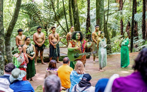 Maori performers in traditional attire with guitar at Te Pā Tū Cultural Experience, New Zealand.