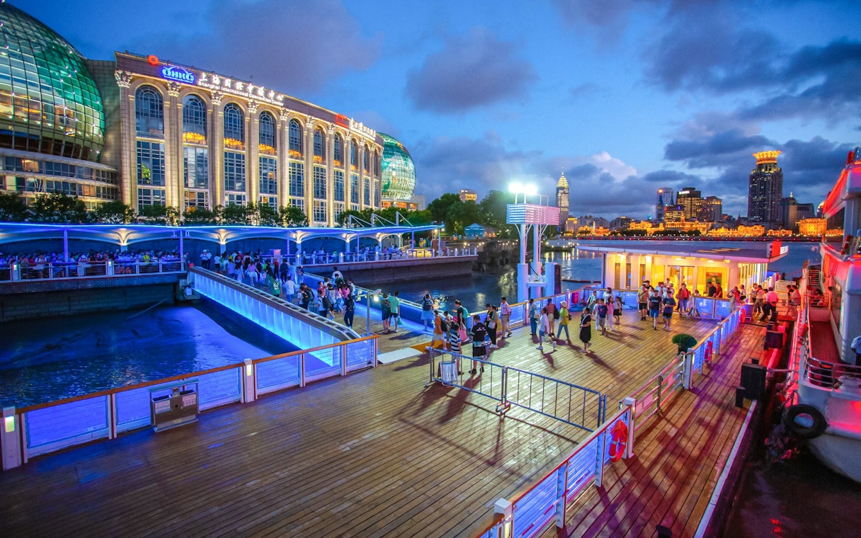 Illuminated cruise port with people boarding near Oriental Pearl Tower, Shanghai.