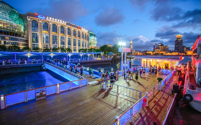 Illuminated cruise port with people boarding near Oriental Pearl Tower, Shanghai.