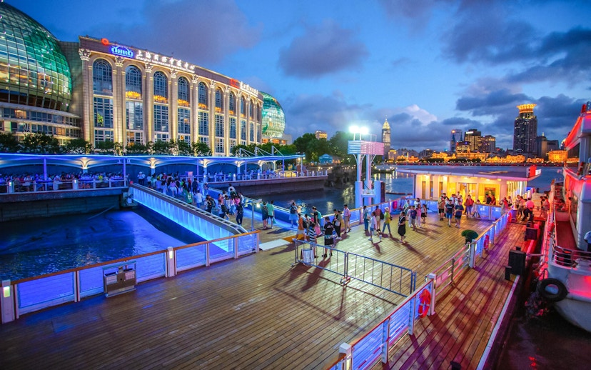 Illuminated cruise port with people boarding near Oriental Pearl Tower, Shanghai.