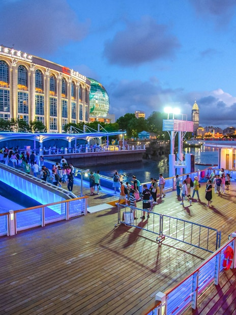 Illuminated cruise port with people boarding near Oriental Pearl Tower, Shanghai.