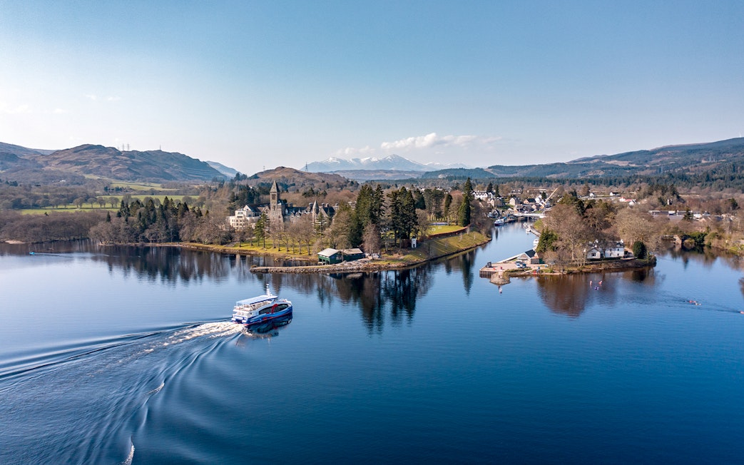 Cruise boat on Loch Ness with scenic views of surrounding hills and village.