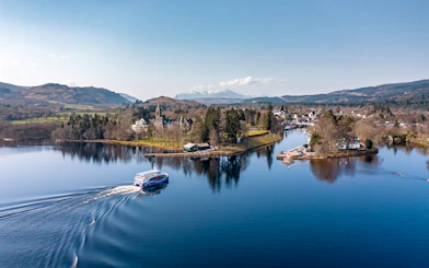 Cruise boat on Loch Ness with scenic views of surrounding hills and village.