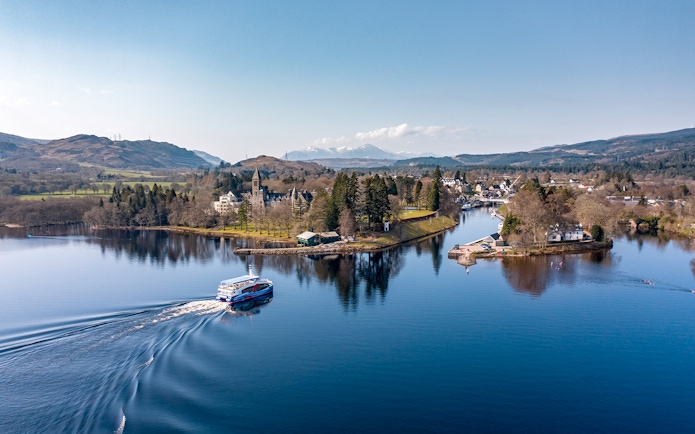 Cruise boat on Loch Ness with scenic views of surrounding hills and village.