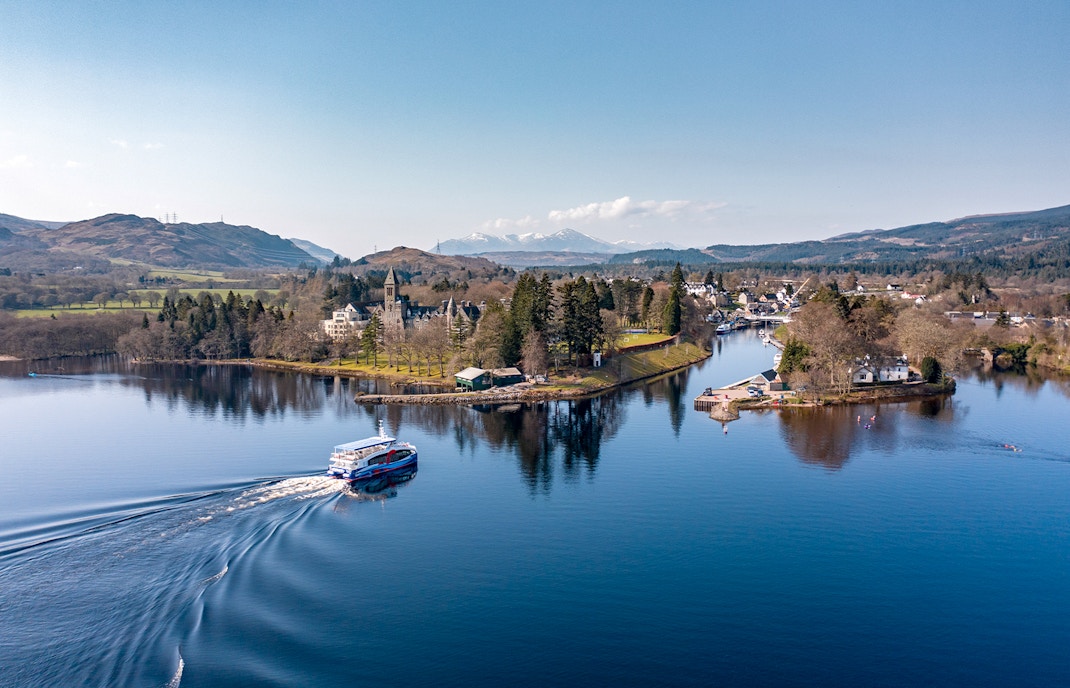 Cruise boat on Loch Ness with scenic views of surrounding hills and village.
