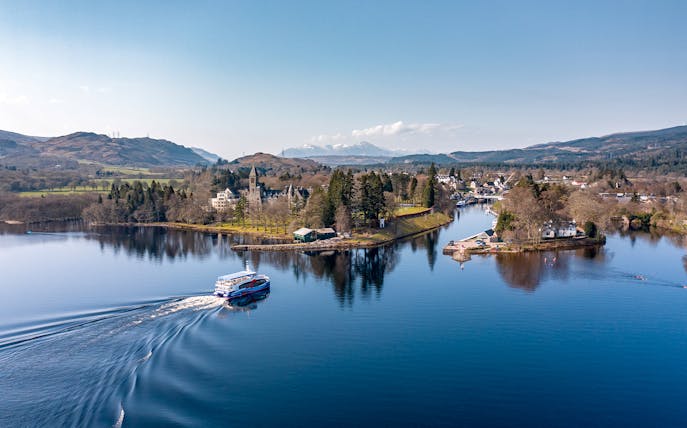 Cruise boat on Loch Ness with scenic views of surrounding hills and village.