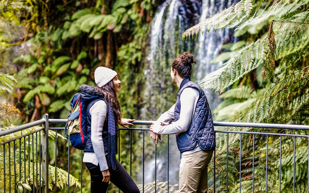 Tourists enjoying a forest walk near a waterfall on the Great Ocean Road day tour.
