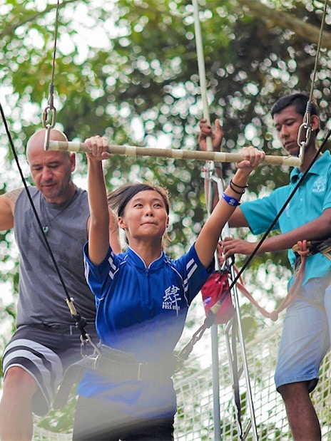 Woman on trapeze at Escape Penang with instructors assisting.