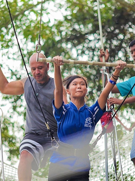 Woman on trapeze at Escape Penang with instructors assisting.