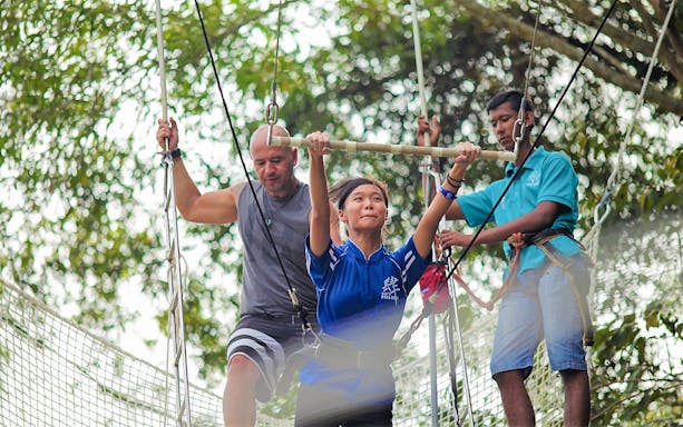 Woman on trapeze at Escape Penang with instructors assisting.