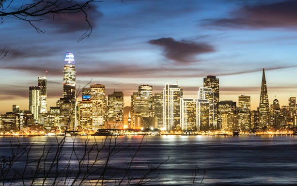 San Francisco skyline at dusk viewed from the bay, featuring illuminated skyscrapers.