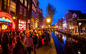 Crowd walking along Amsterdam's Red Light District canal at night.