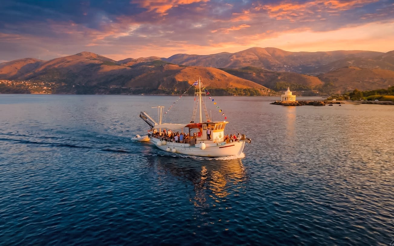 Sunset cruise boat on the sea near Kefalonia with mountains and lighthouse in the background.