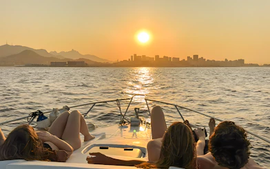 Tourists relaxing on a boat during a Rio de Janeiro sunset cruise with city skyline in view.