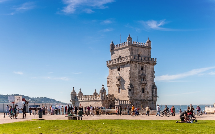Belem Tower in Lisbon with tourists and cyclists nearby.