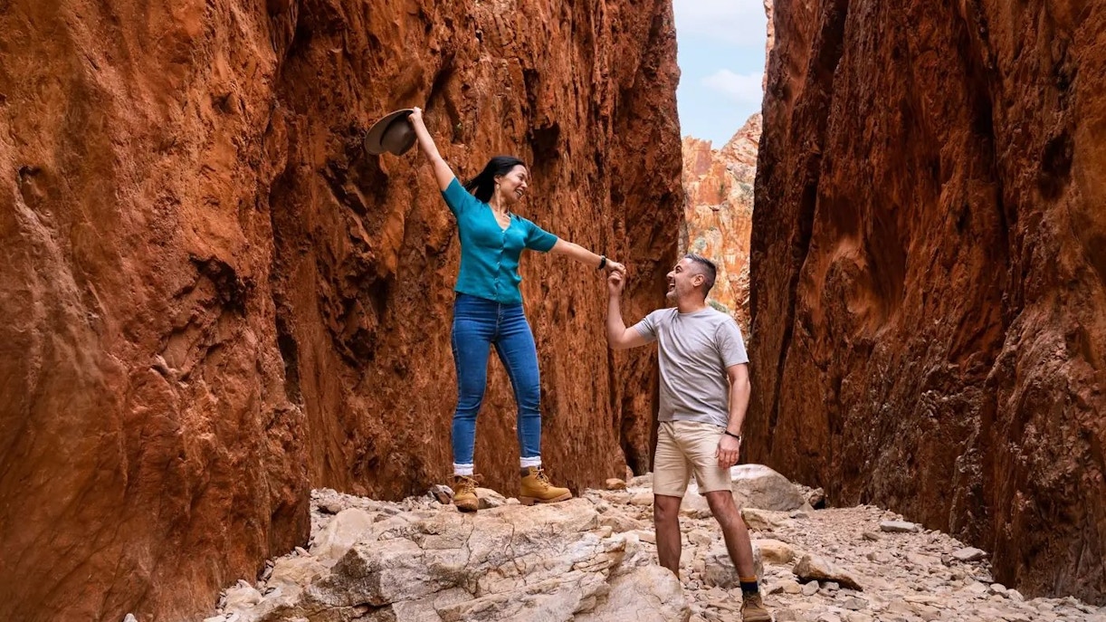 Couple exploring narrow red rock gorge on Uluru–Kata Tjuta camping tour.